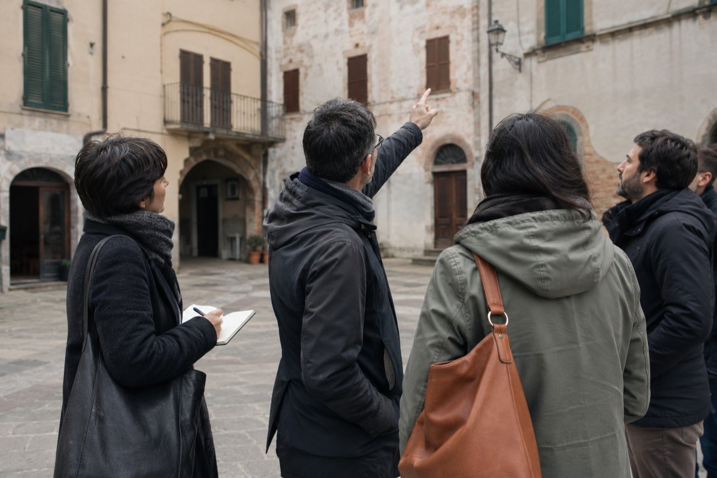Un gruppo osserva gli edifici di una piazza durante una visita sul territorio