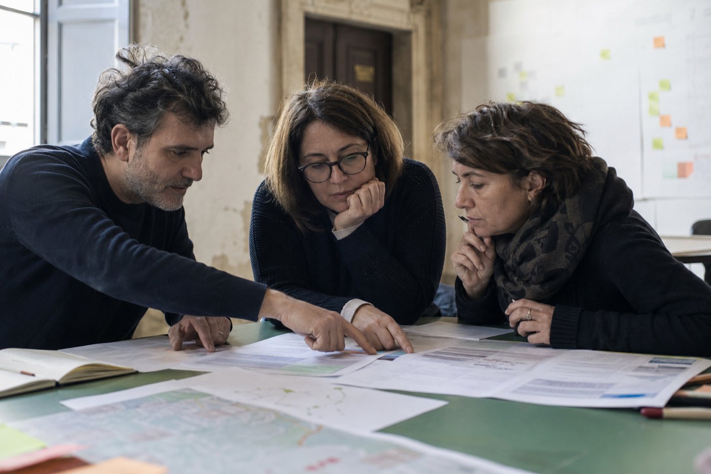 Tre persone studiano insieme dati e mappe stampate durante una valutazione